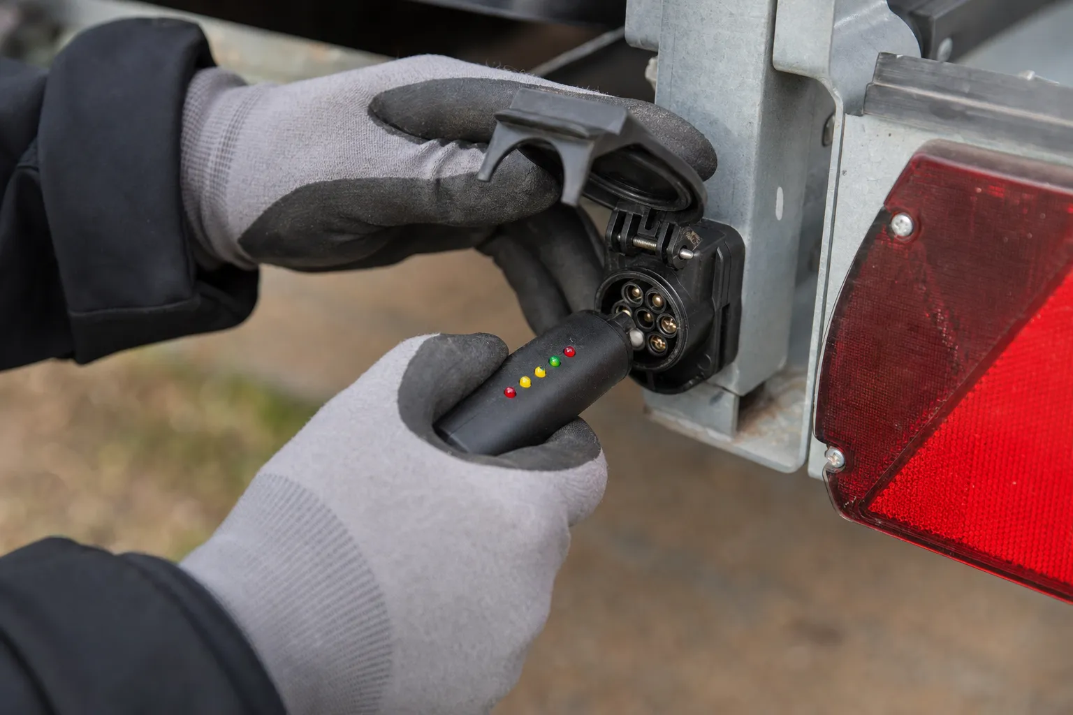 Gloved hands testing a trailer wiring connector